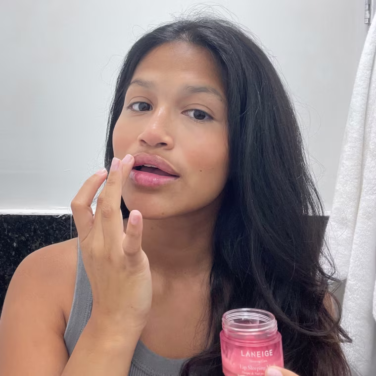 Woman applies Laneige Lip Sleeping Mask directly onto her lips using her fingers in the bathroom.
