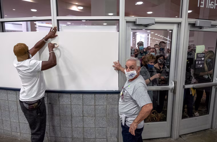 Poll workers hang up white paper to block off windows.
