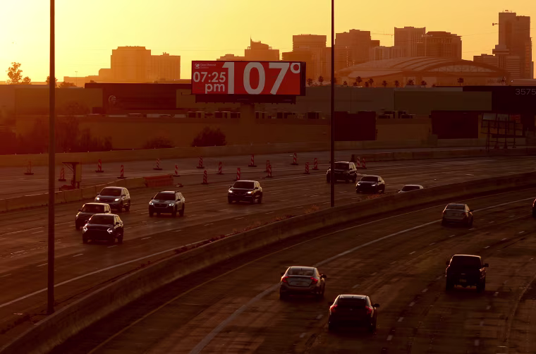 A billboard over a highway with cars and a setting sun