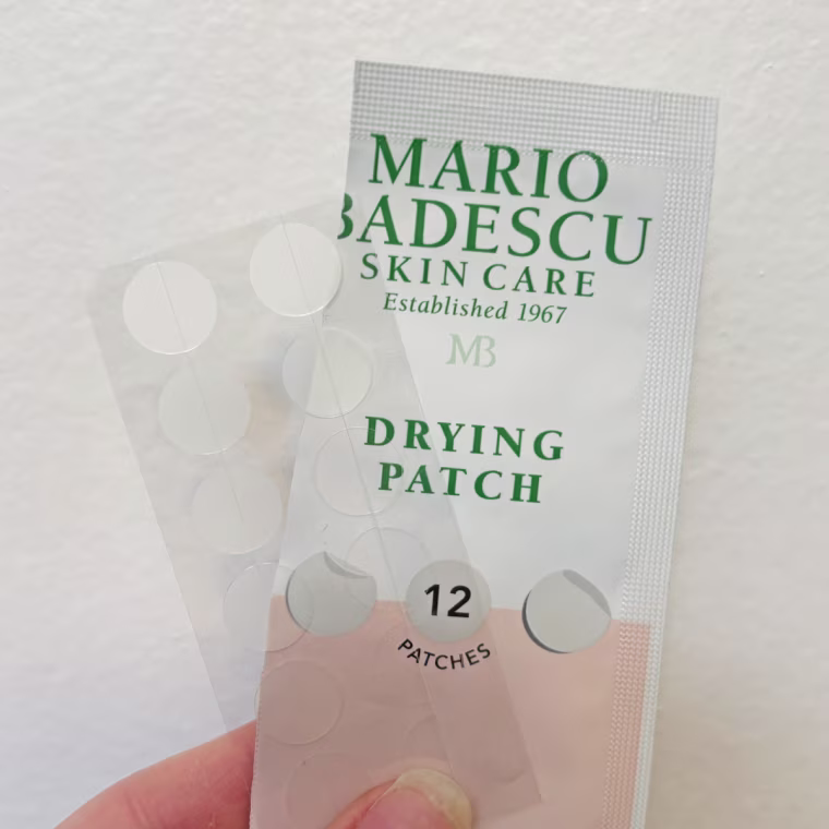 Woman holds the packaging and sheet of pimple patches in her hand.