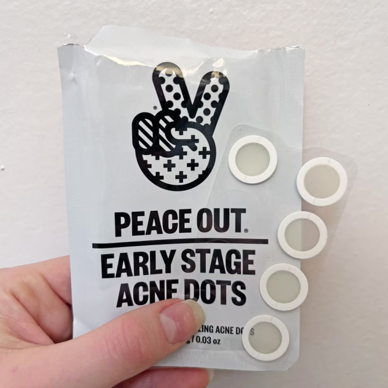 Woman holds the packaging and sheet of pimple patches in her hand.