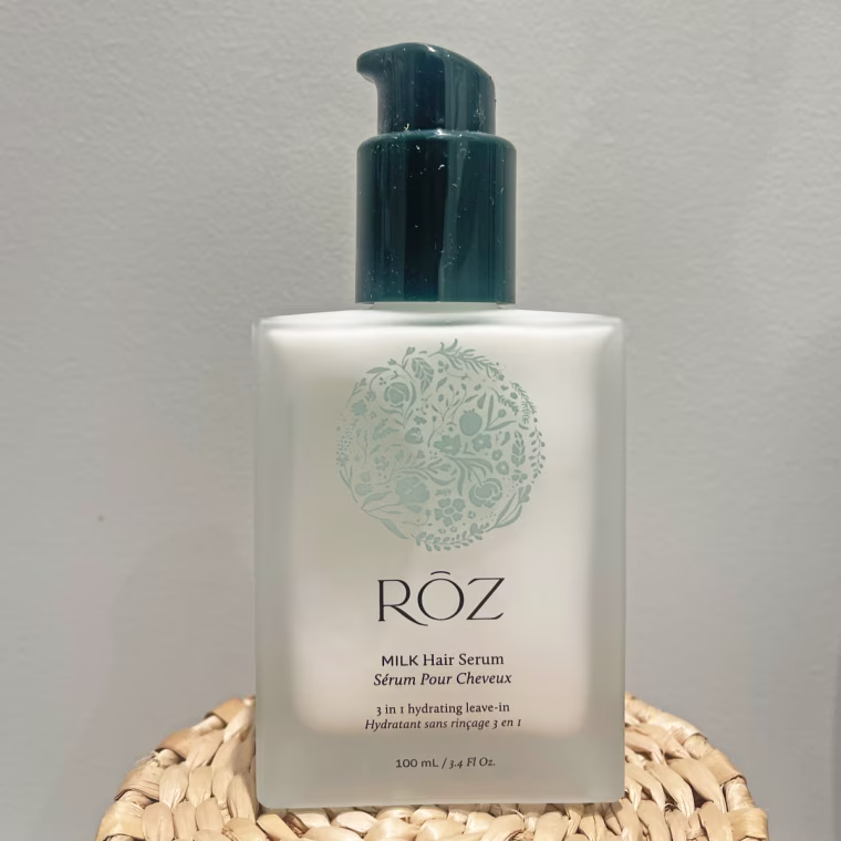 A bottle of Roz Milk Hair Serum sits on top of a wooden coaster.