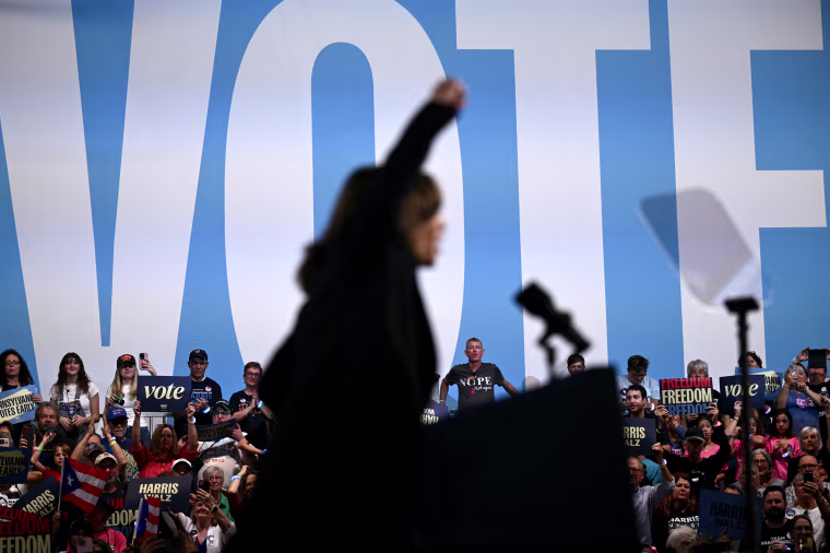 Kamala Harris raises her fist in front of supporters and a large "Vote" sign
