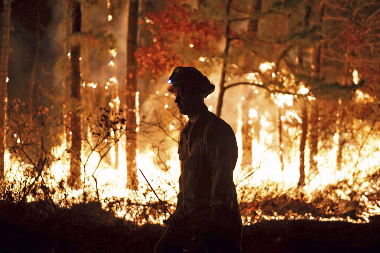 A firefighter is silhouetted against a forest fire on Wednesday, Nov. 6, 2024 in Evesham, N.J.
