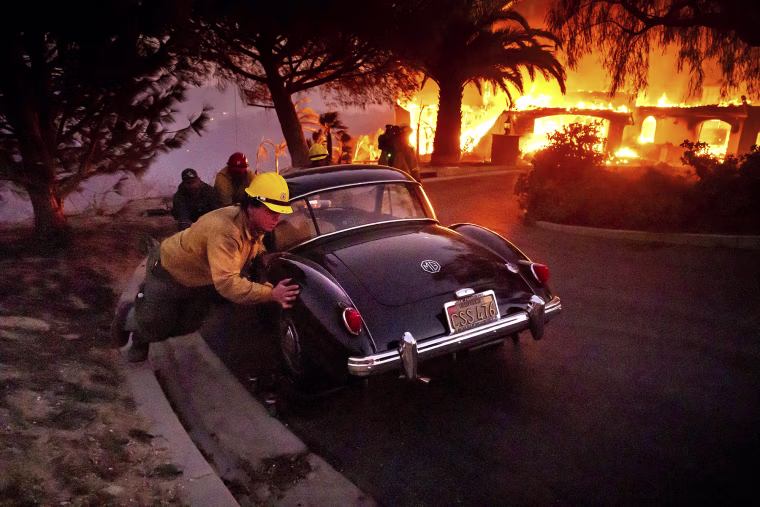 Firefighters and sheriff's deputies push a vintage car away from a burning home