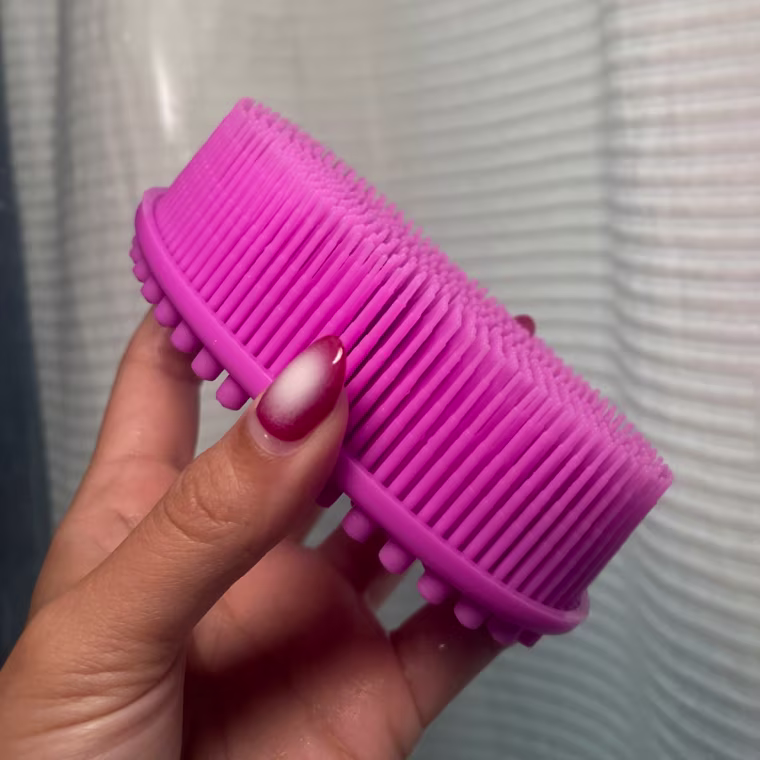 Woman holding pink silicone scrubber against shower curtain