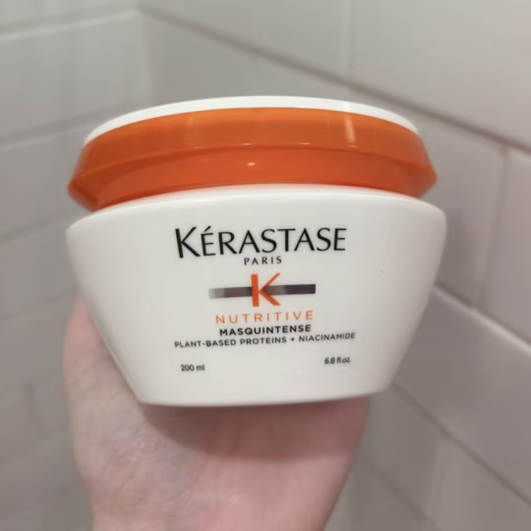Woman holds Kérastase Nutritive Masquintence Hair Mask in her hand.