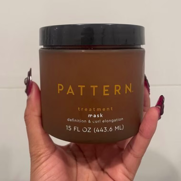 Woman holds up the Pattern Treatment Hair Mask in her hand against a wall.