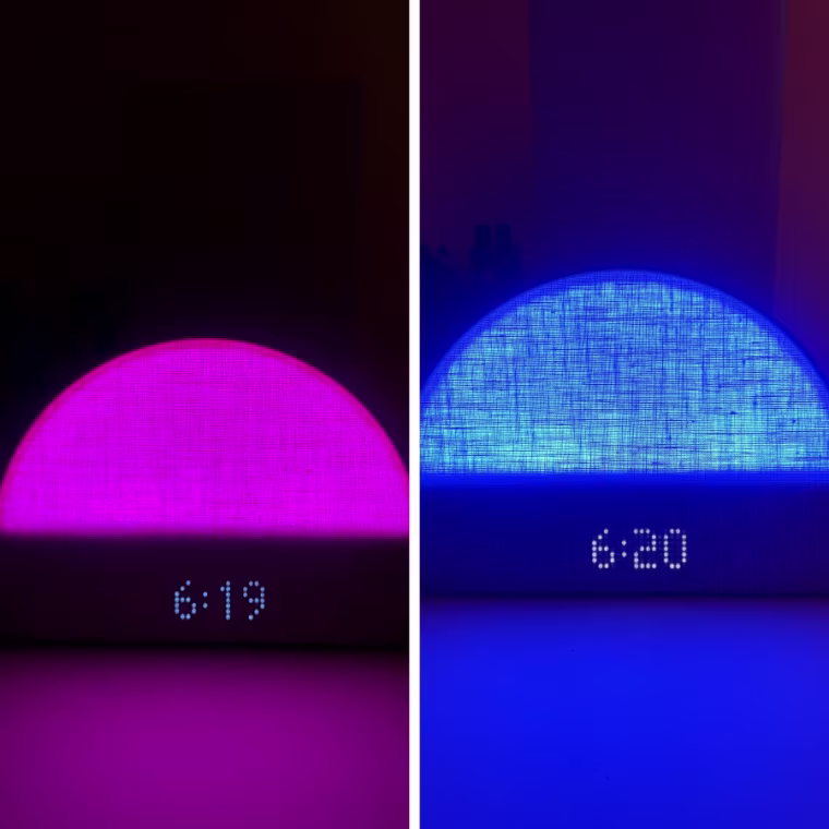 Hatch Restore 2 on a table in the dark, lit up pink with the time 6:19 on the display.
Right - Hatch Restore 2 on a table in the dark, lit up blue with the time 6:20 on the display.
