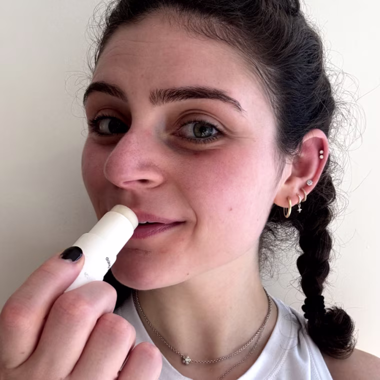 Woman applying white tube of sheer lip balm