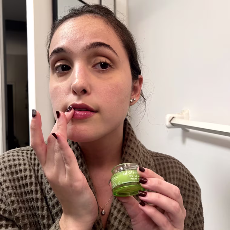 Woman in green robe applying sheer lip balm to lips