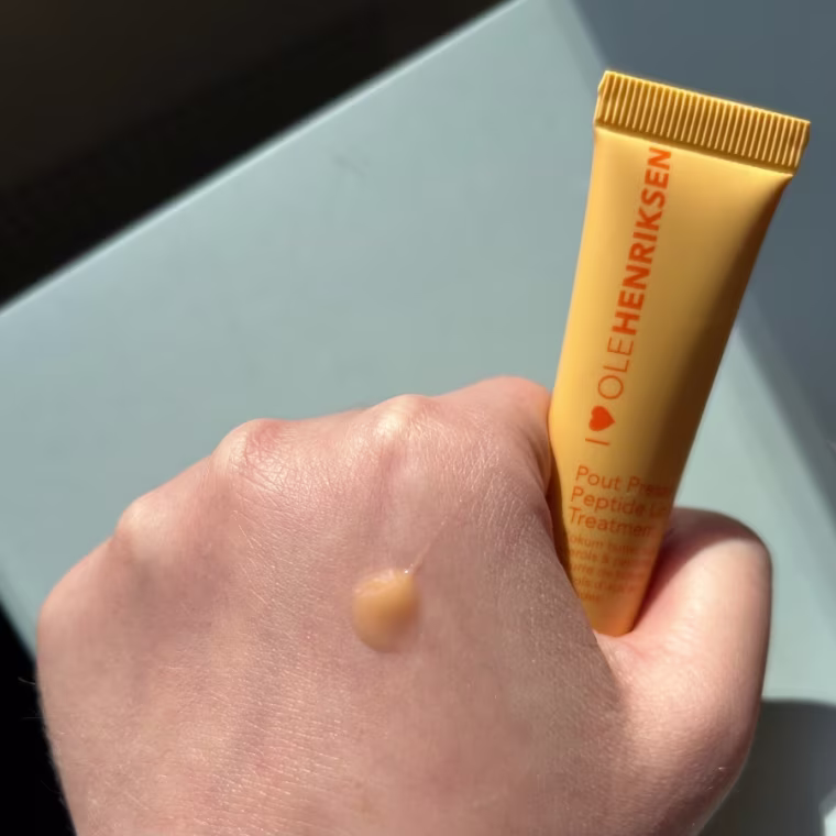 Woman holding lip balm with an orange-tinted swatch on her hand