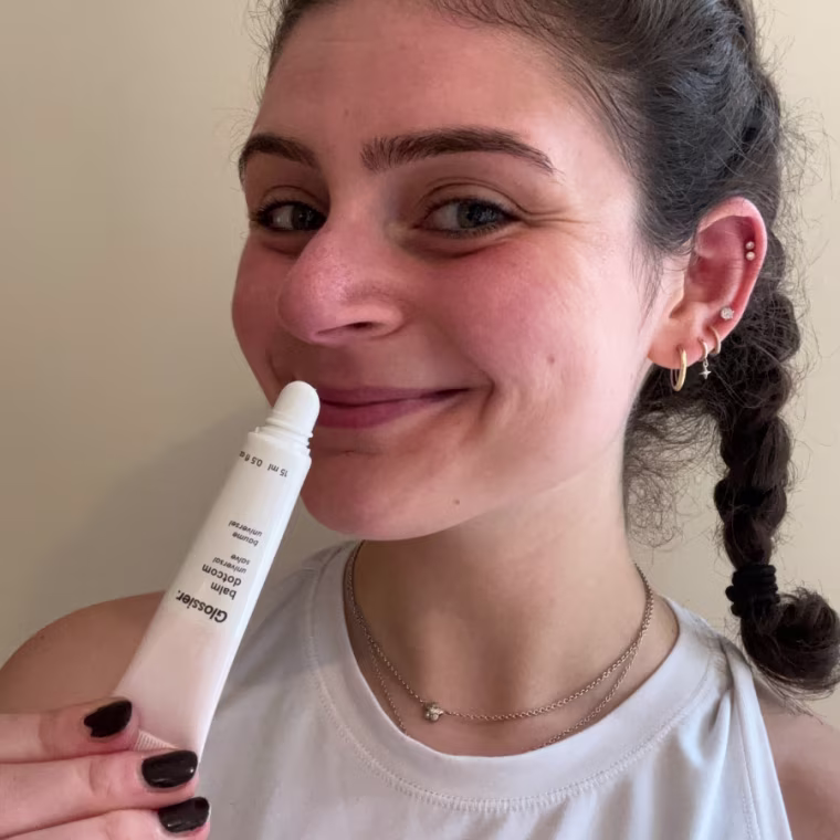 Woman applying pink and white tube of sheer lip balm to lips