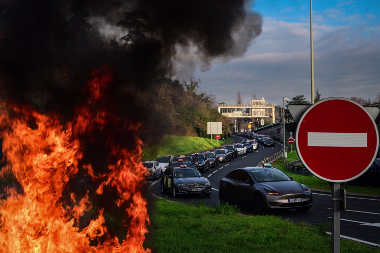 A fire is seen as taxi drivers block the roads during a demonstration against a new downward pricing system for medical transport and a "shared taxi" obligation proposed by the Caisse Nationale d'Assurance Maladie (CNAM), in Lyon central-eastern France on December 2, 2024. Several hundred taxi drivers began slowing down or blocking several access points to the Lyon metropolitan area on December 2, 2024 morning, to protest against the agreement being negotiated with the French health insurance scheme for the transport of seated patients, according to the Rhone prefecture.