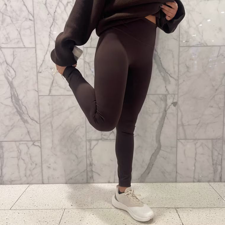 Woman stretches wearing brown Alo ⅞ High-Waist Airlift leggings.