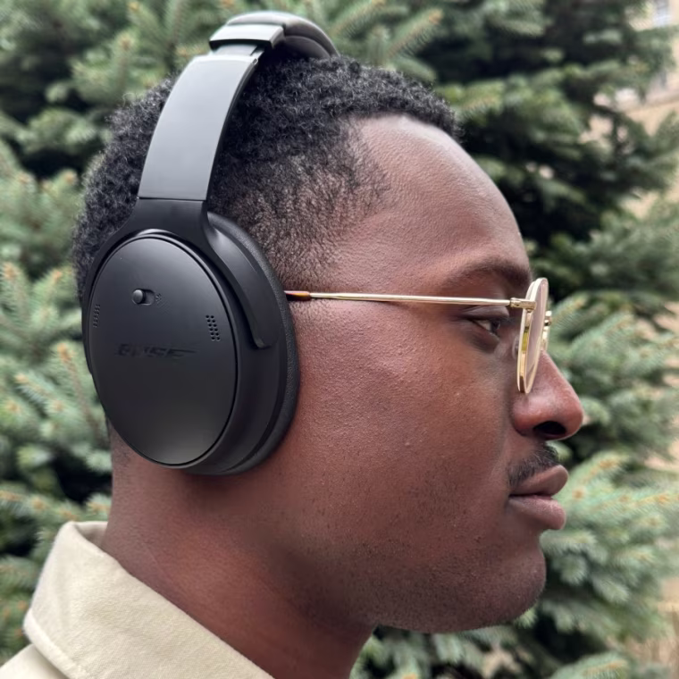 In-profile shot of NBC Select commerce editor Jordan Bowman wearing the Bose QuietComfort headphones with a green tree in the background.