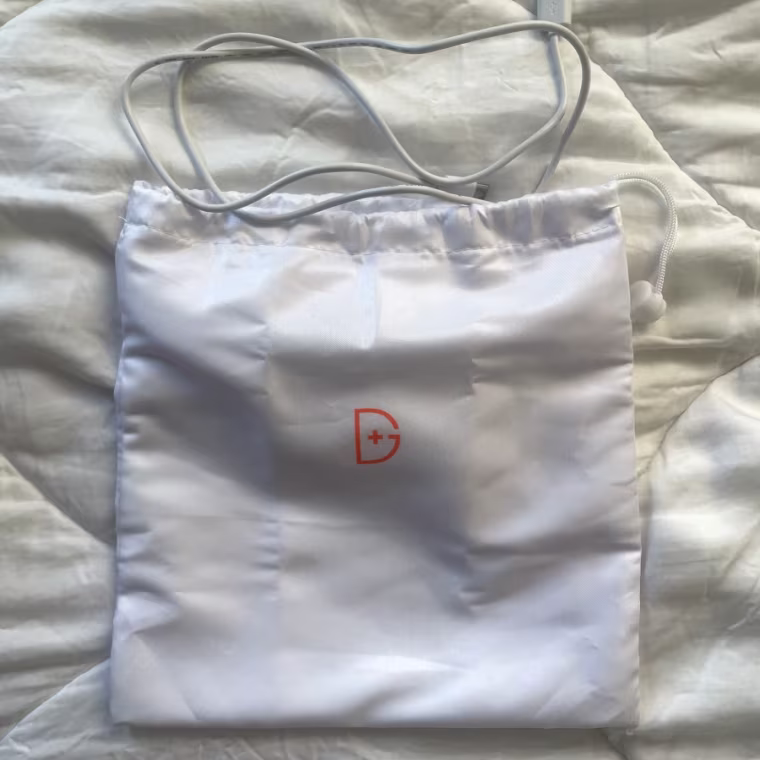 A satin bag and a white charger cord laying against a white bedspread