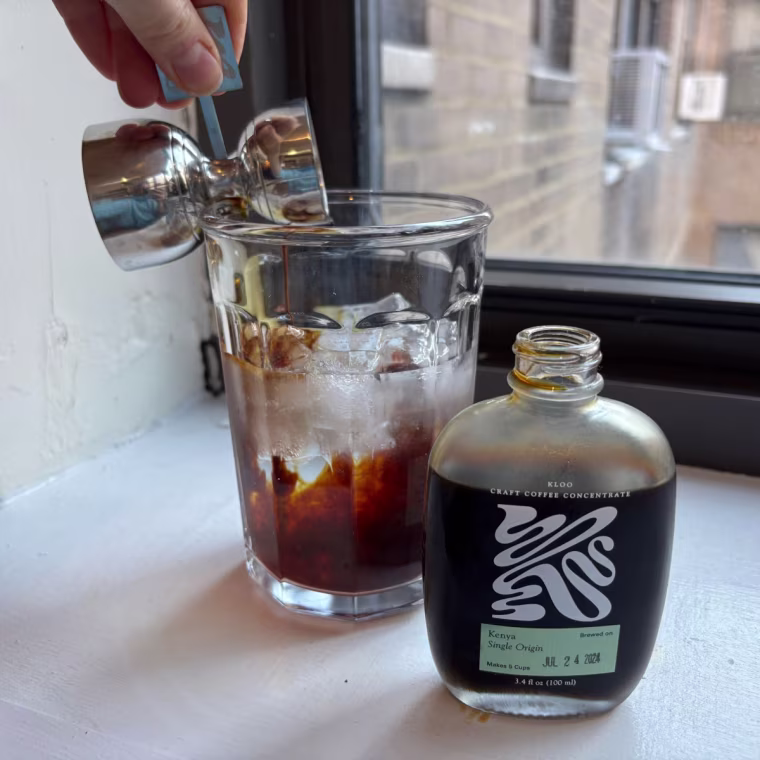 Woman pouring coffee into glass cup with Kloo coffee concentrate bottle on the side