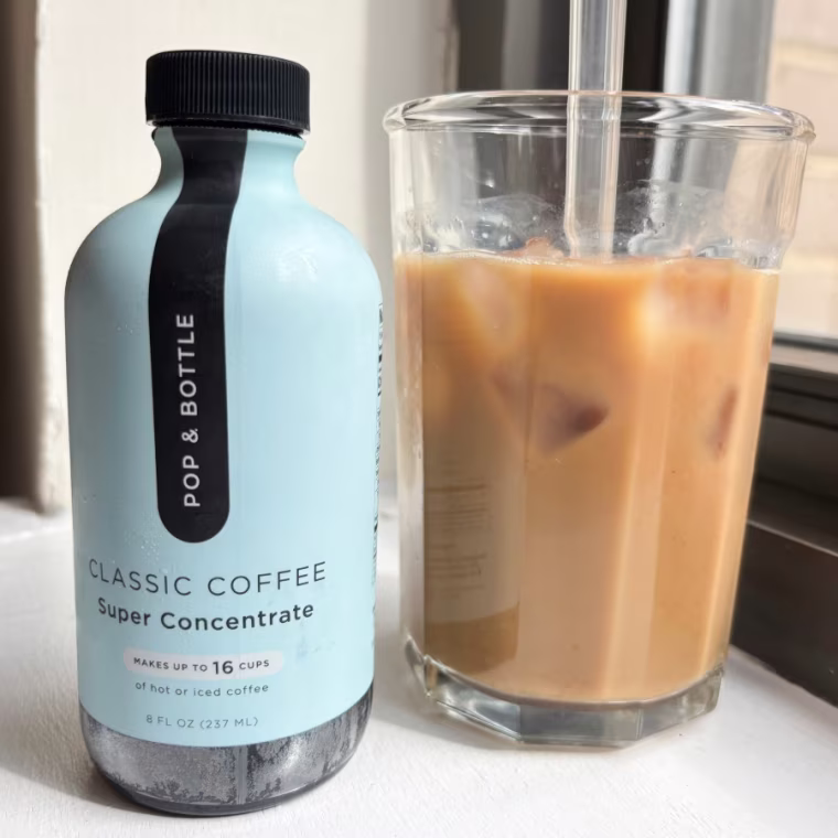Bottle of Pop & Bottle coffee concentrate next to a glass cup of coffee with straw