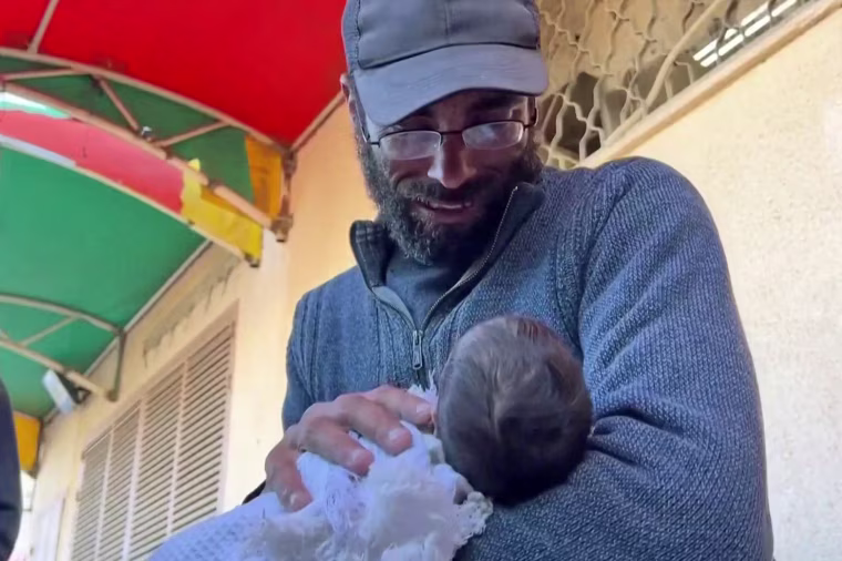 Yahya Al-Batran holds the motionless body of his newborn baby, Jumaa, wrapped up in a blanket.