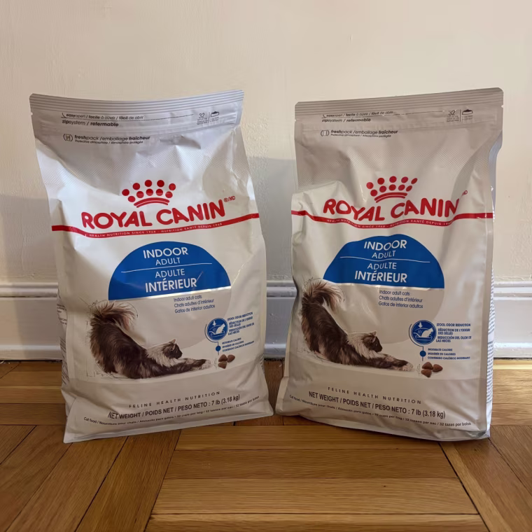 Two bags of Royal Canin dry cat food standing up next to each other against a white wall.