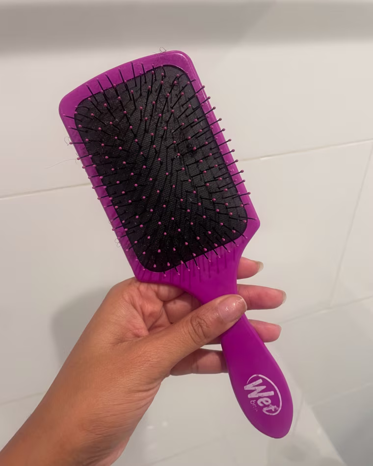 Woman holding purple hairbrush against white wall