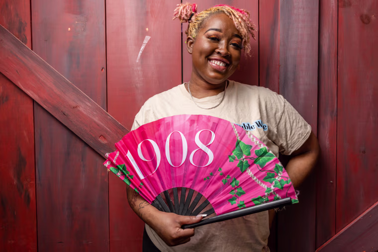 Alexus Sumpter holds a pink fan that reads "1908"