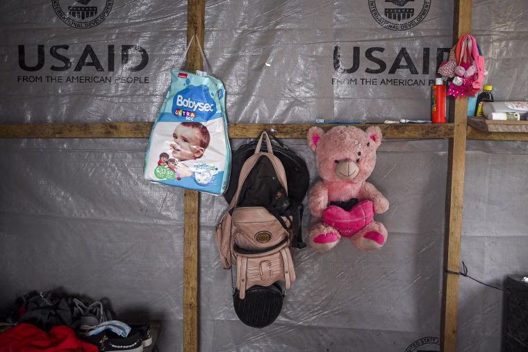 A wall with purses, diapers and a teddy bear.