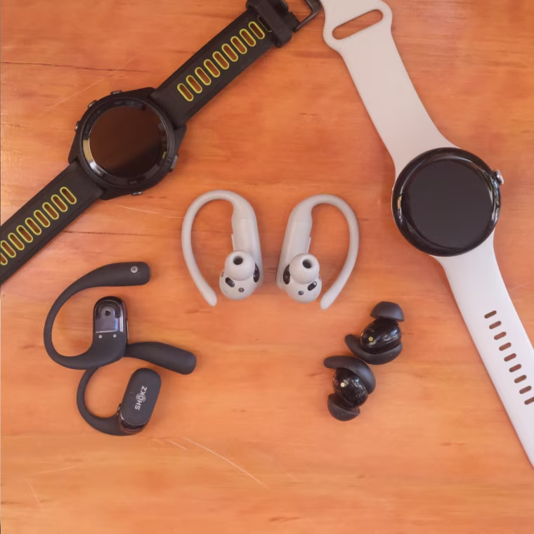 A close up image of a variety of headphones and smartwatches against a wood background.
