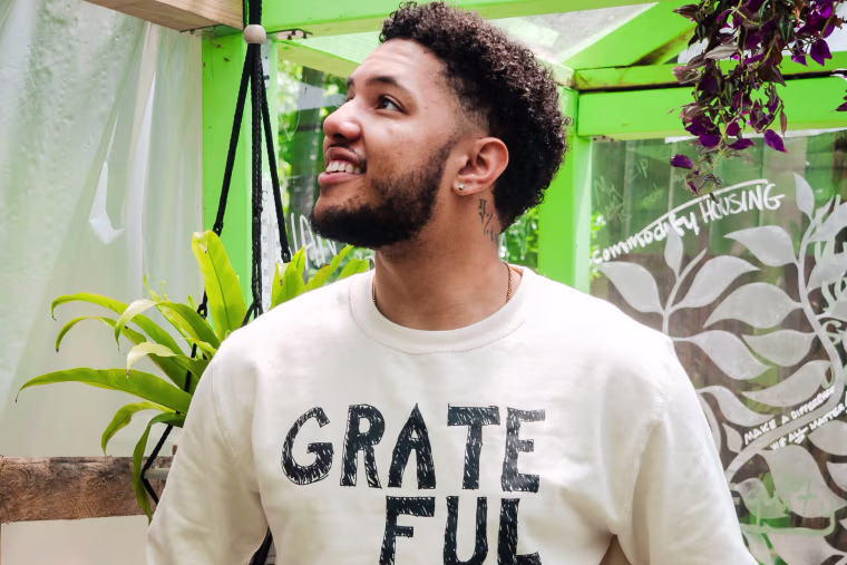 A man wears a beige sweatshirt that says "Grateful" in black text