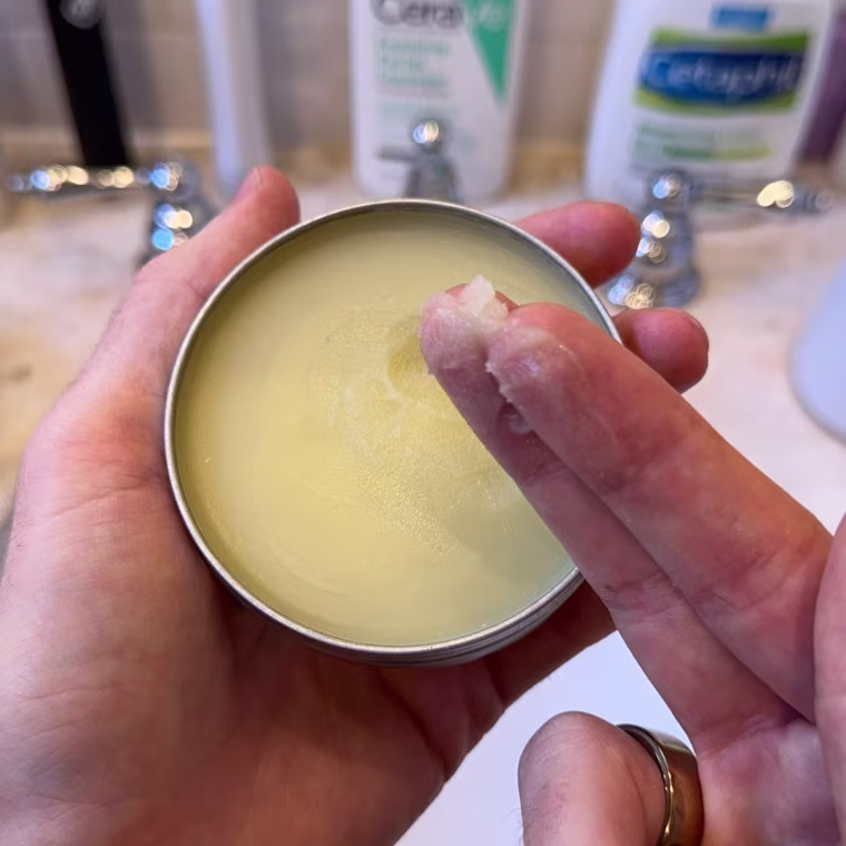 Man holding Burt’s Bees beard balm with a portion on his fingers.