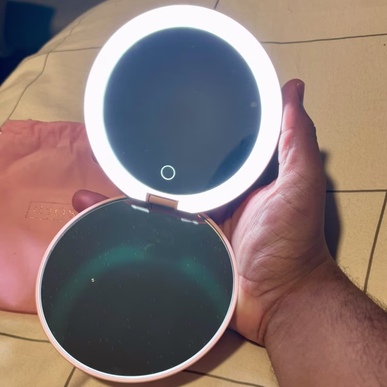 Small round LED mirror lit on a bed.