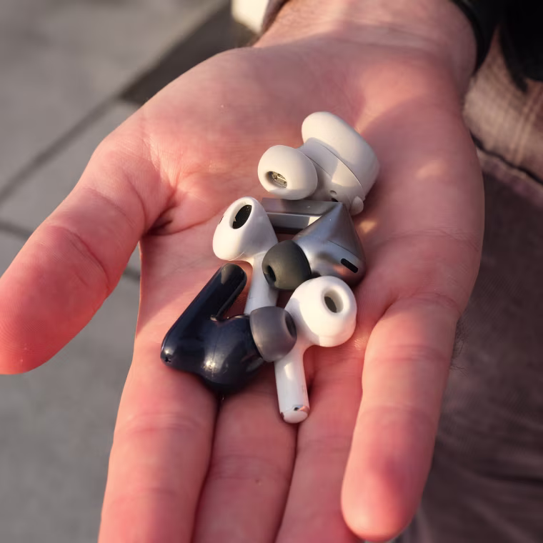 A close up of the writer’s hand holding five different earbuds, including the Apple AirPods 4