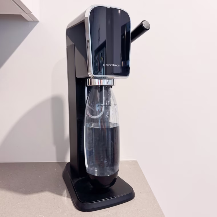 Sodastream Art sitting on a countertop beside a cabinet.
