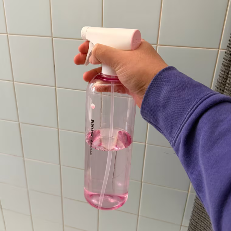 Person holding Blueland bathroom spray in front of tile wall.