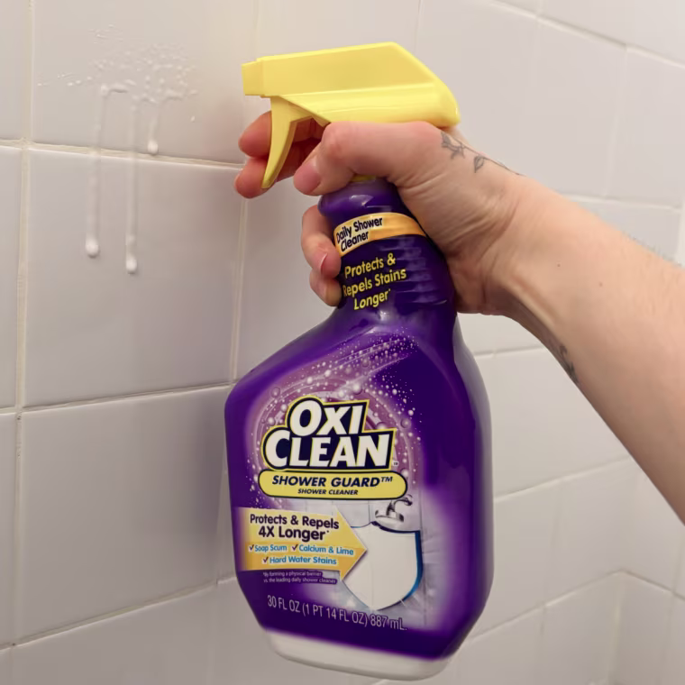 Person holding bottle of Oxiclean Shower Guard spray in front of a tile wall.