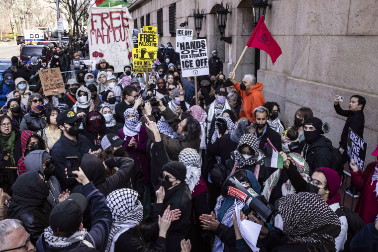 Demonstrators hold signs and flags and wear headscarves and masks.