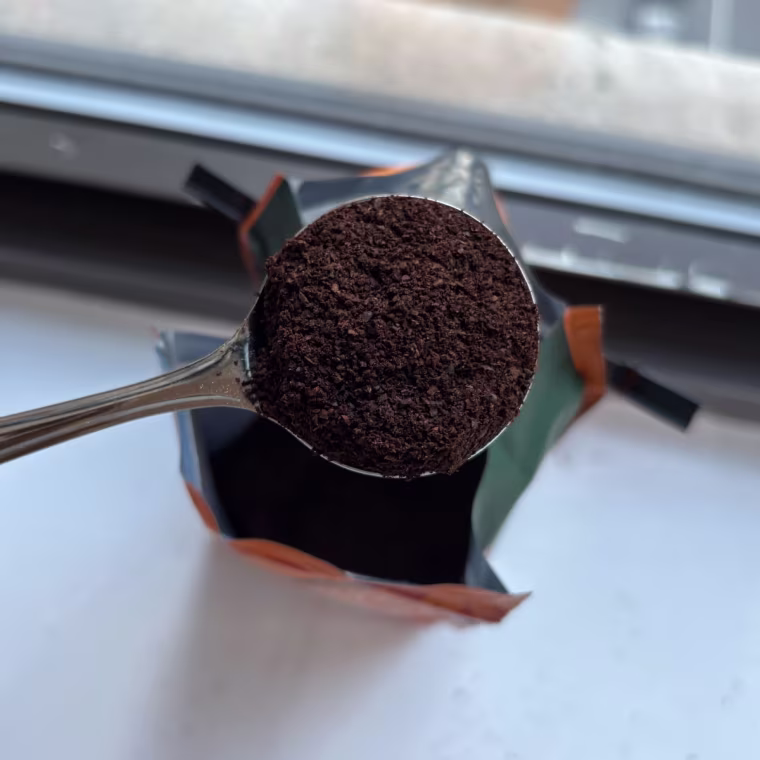 A hand holding a metal scoop filled with Four Sigmatic Focus Organic Mushroom Coffee grounds.