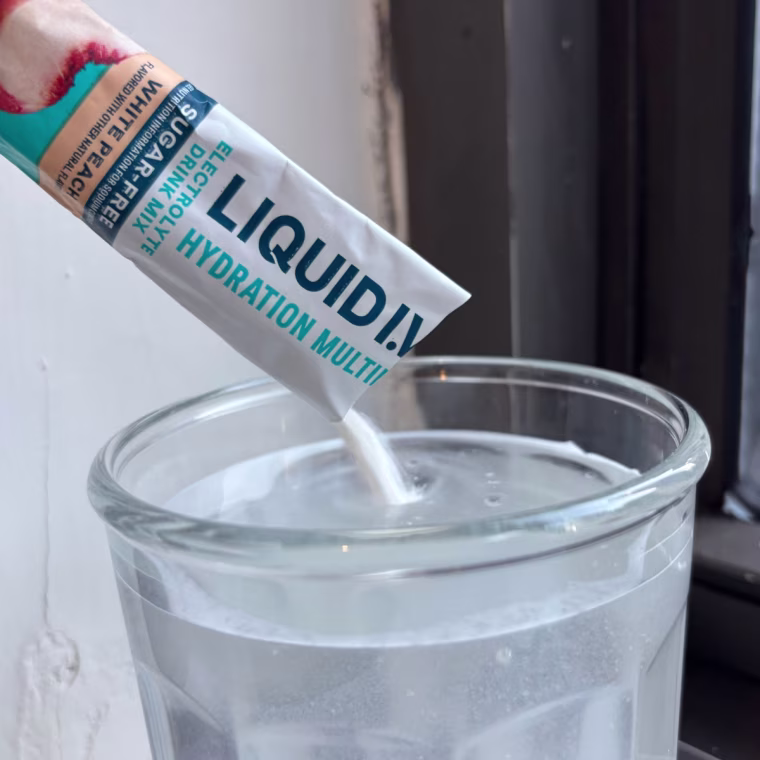 Person pouring packet of electrolyte powder into a cup of water.