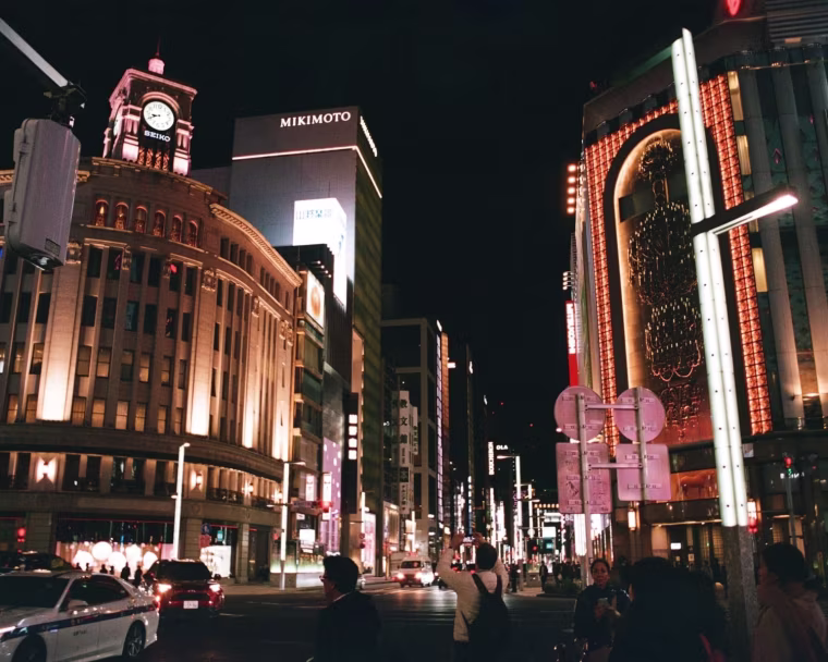 A photo of a busy street at night, flanked by tall, illuminated buildings.