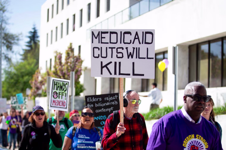 A person outside in a crowd holds a sign that says "Medicaid cuts will kill"