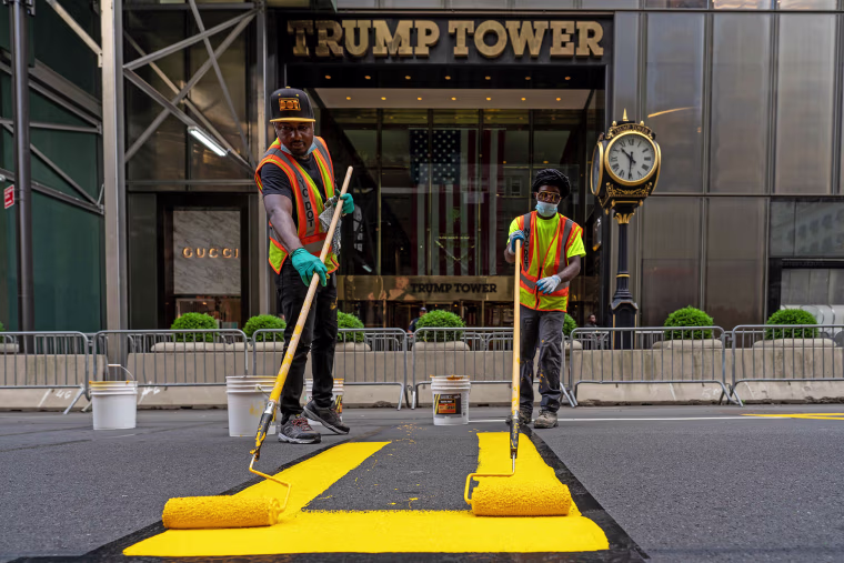 Two people painting a yellow 'Black Lives Matter' mural on Fifth Avenue directly in front of Trump Tower in New York