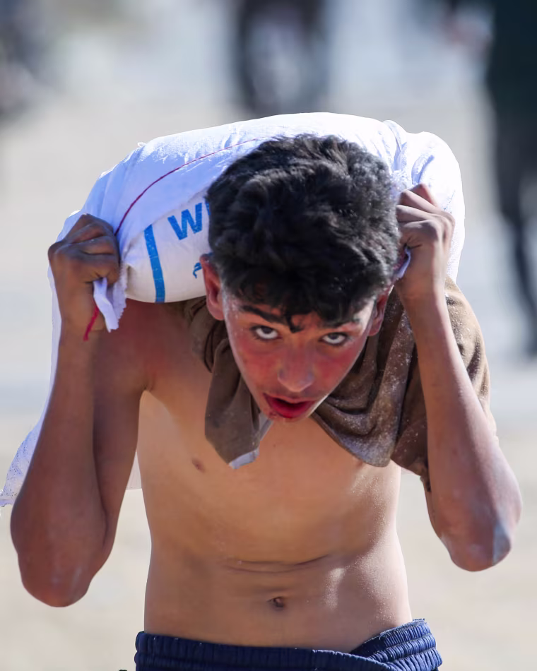 A young boy carries a bag of food aid on his shoulders 