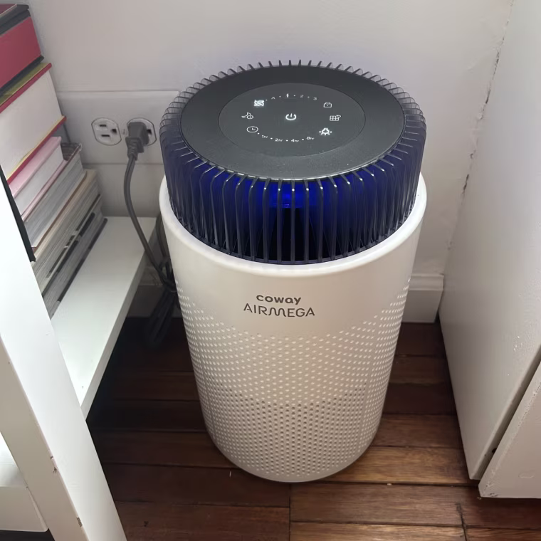 A photo of the Coway Airmega 100 air purifier plugged into the corner of a room.
