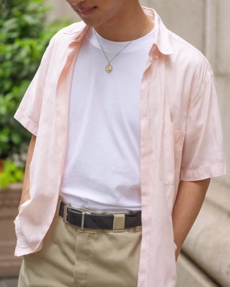 A close shot of a model wearing a white t-shirt paired with a pink colored button down shirt.