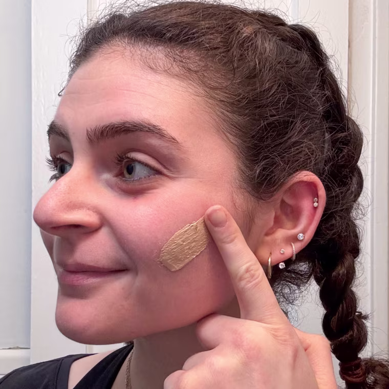 A woman applying Naturium’s Dew-Glow Tinted Moisturizer SPF 50+.