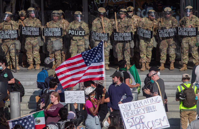 Demonstrators holding signs and flags face California National Guard members standing guard outside the Federal Building
