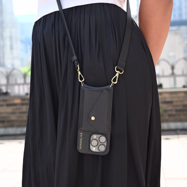 A close up of a woman wearing a Bandolier Hailey phone case, which hangs against her black skirt.