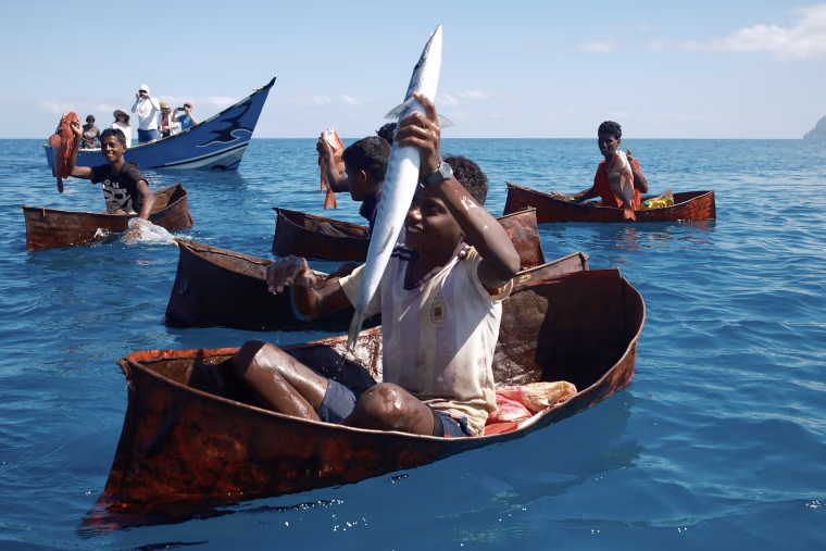 Children catch fish using only a hook and line in boats made from welded oil drums.