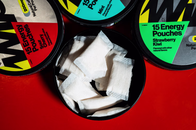 Wip containers displayed on a red table, one of the containers is open and shows white pouches filled with powder inside